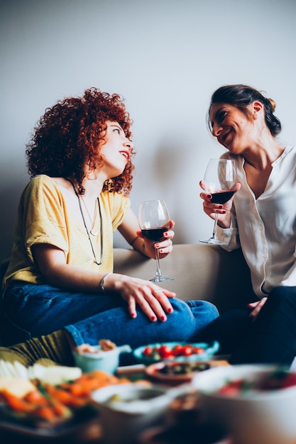 Photo friends with wineglasses talking while sitting on sofa at home