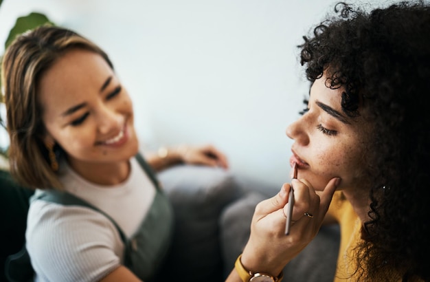 friends woman and relax with makeup in home with closeup for cosmetics beauty and wellness young people helping and apply lipstick with hand by holding product and peace in happy with precision
