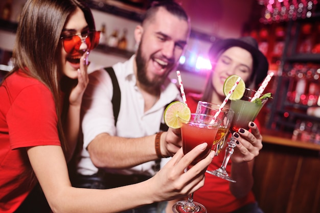 Friends-young guy and two cute girls having fun at a party holding cocktails