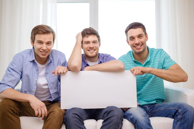 friendship and advertising concept - smiling male friends holding white blank board