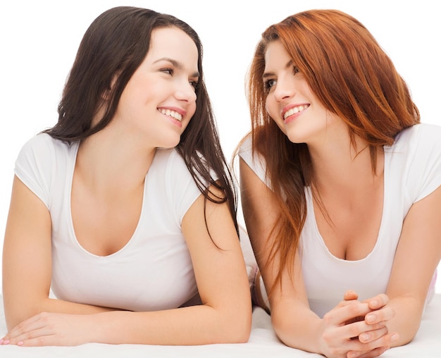 우정과 행복한 사람들 개념 - 서로를 바라보는 흰색 티셔츠를 입은 두 명의 웃는 소녀