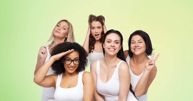 friendship, beauty, body positive and people concept - group of happy plus size women in white underwear having fun and making faces over green natural background