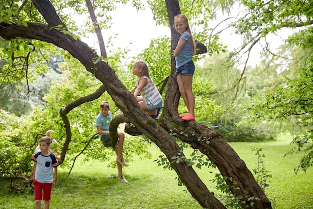 友情、幼年期、余暇、人のコンセプト – 幸せな子供や友人のグループが木に登り、夏の公園で楽しむ