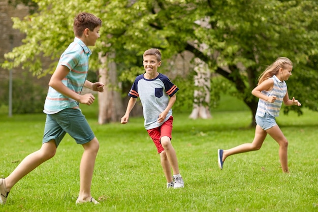 friendship, childhood, leisure and people concept - group of happy kids or friends playing catch-up game and running in summer park