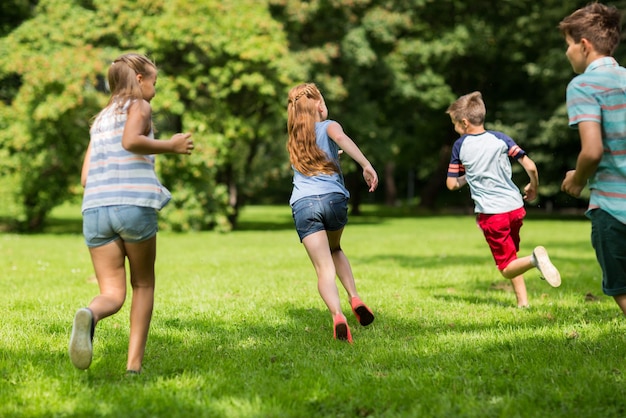 Концепция дружбы, детства, досуга и людей - группа счастливых детей или друзей, играющих в игры и бегущих в летнем парке