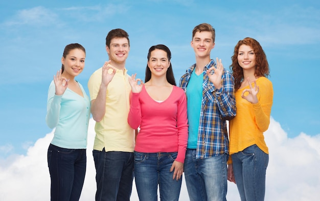 friendship, dream, future and people concept - group of smiling teenagers showing ok sign over blue sky with white cloud background