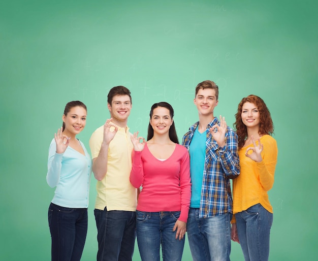 friendship, education, school and people concept - group of smiling teenagers showing ok sign over green board background