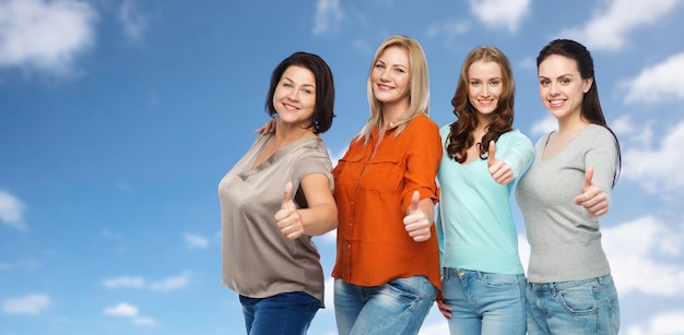 friendship, fashion, body positive, gesture and people concept - group of happy different size women in casual clothes showing thumbs up over blue sky and clouds background