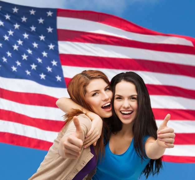 Foto concetto di amicizia e persone felici - due ragazze sorridenti che mostrano i pollici in su sullo sfondo della bandiera americana