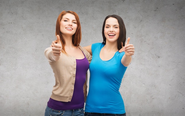 friendship and happy people concept - two smiling girls showing thumbs up