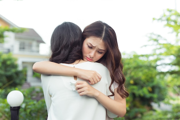 友情ヘルプ サポート。落ち込んでいるアジアの女性が友達を抱きしめている。