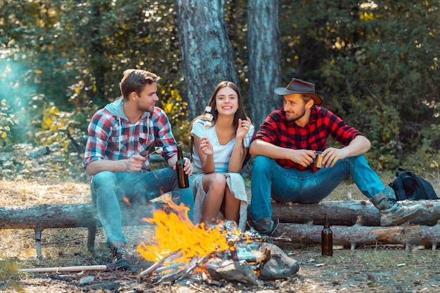 Friendship and leisure concept Friends hikers watching fire together on camp Weekend Good day for spring picnic in nature Beautiful young friends enjoying picnic in a park