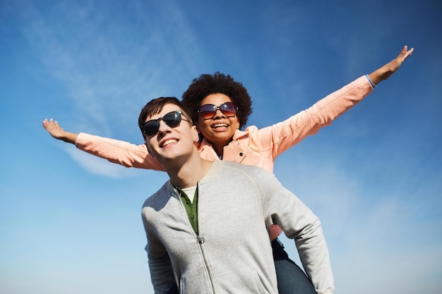 friendship, leisure, international, freedom and people concept - happy teenage couple in shades having fun outdoors