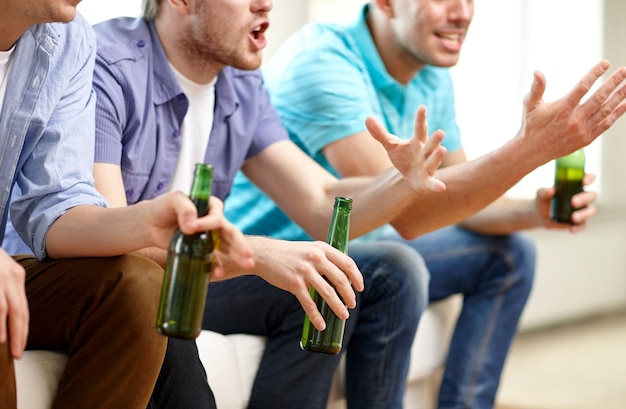 концепция дружбы, отдыха, людей и алкоголя - крупный план счастливых друзей-мужчин, пьющих пиво и смотрящих телевизор дома