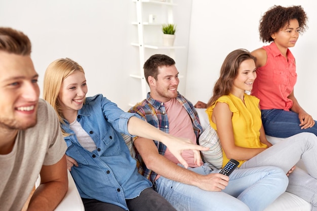 friendship, leisure, people and entertainment concept - happy friends with remote watching tv at home