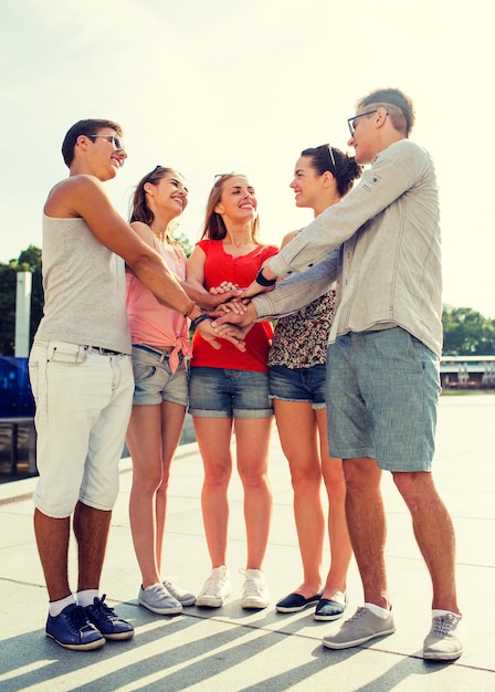 Concetto di amicizia, tempo libero, estate, gesto e persone - gruppo di amici sorridenti con le mani in cima in città