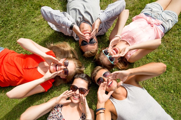 friendship, leisure, summer and people concept - group of smiling friends lying on grass in circle outdoors