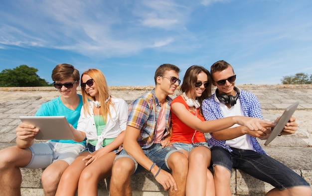 friendship, leisure, summer and people concept - group of smiling friends with tablet pc computers sitting outdoors