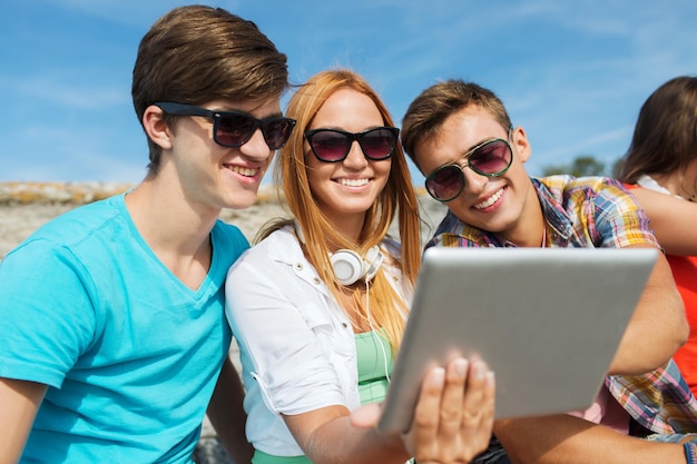 Concetto di amicizia, tempo libero, estate, tecnologia e persone - gruppo di amici sorridenti con computer tablet pc seduti all'aperto