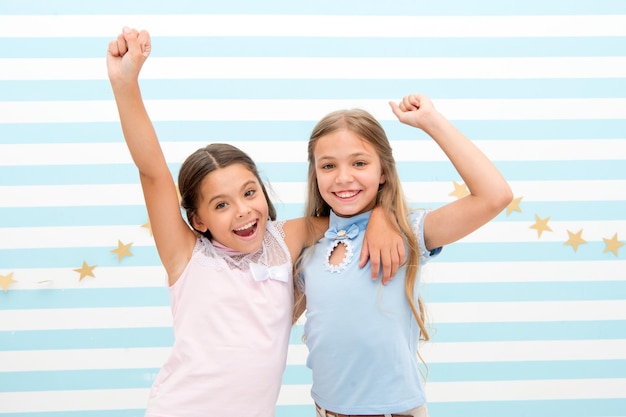 Friendship makes us rich Kids schoolgirls preteens happy together Friendship from childhood Girls smiling happy faces hug each other stand striped background Girls children best friends hug