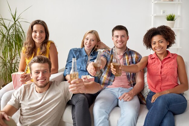 friendship, people and holidays concept - happy friends with popcorn drinking beer at home