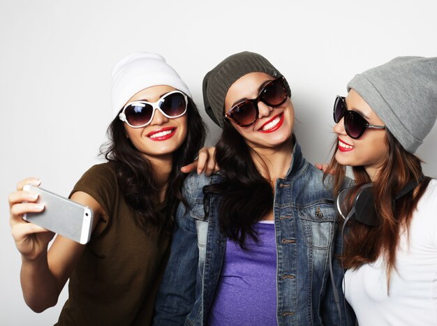 Friendship, people and technology concept - three happy teenage girls with smartphone taking selfie