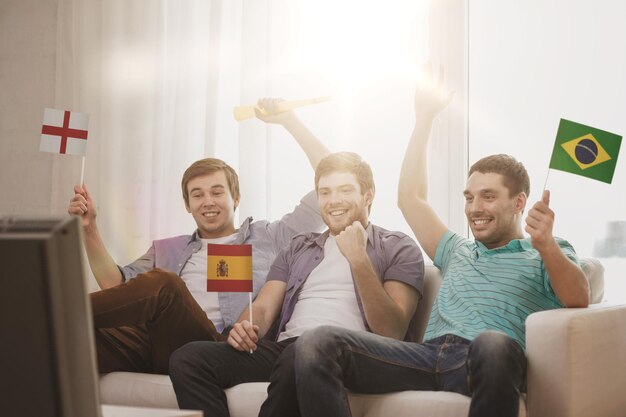 friendship, sports and entertainment concept - happy male friends with flags and vuvuzela supporting football team at home