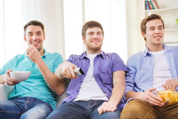 友情、スポーツ、エンターテインメントの概念-家でテレビを見ている軽食を持つ幸せな男性の友人