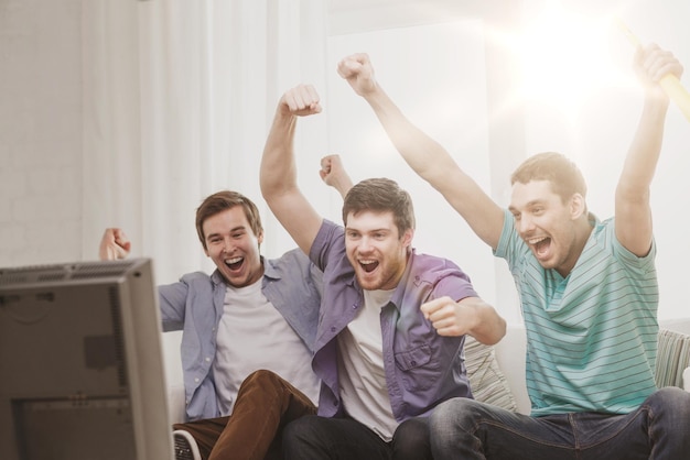 friendship, sports and entertainment concept - happy male friends with vuvuzela watching sports on tv