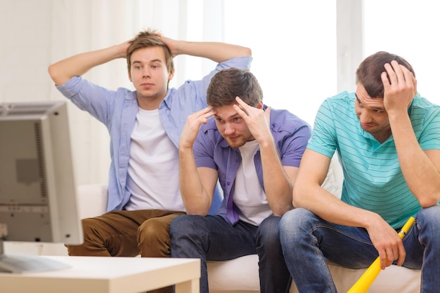 friendship, sports and entertainment concept - sad male friends with vuvuzela watching sports on tv at home