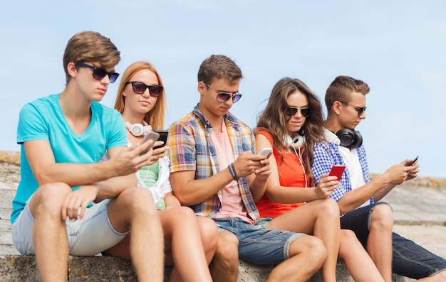 friendship, summer, technology and people concept - group of friends with smartphones and headphones outdoors