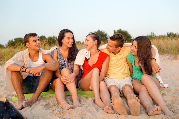 우정, 여름 휴가, 휴일, 몸짓, 그리고 사람들의 개념 - 해변에 앉아 웃고 있는 친구들