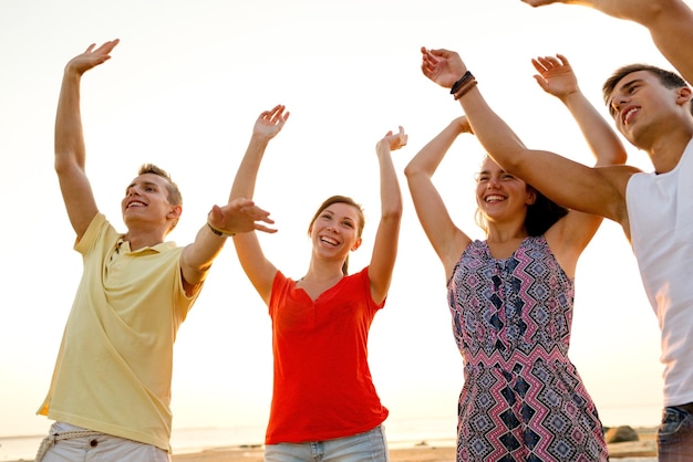 friendship, summer vacation, holidays, party and people concept - group of smiling friends dancing on beach