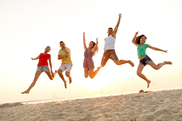 friendship, summer vacation, holidays, party and people concept - group of smiling friends dancing and jumping on beach