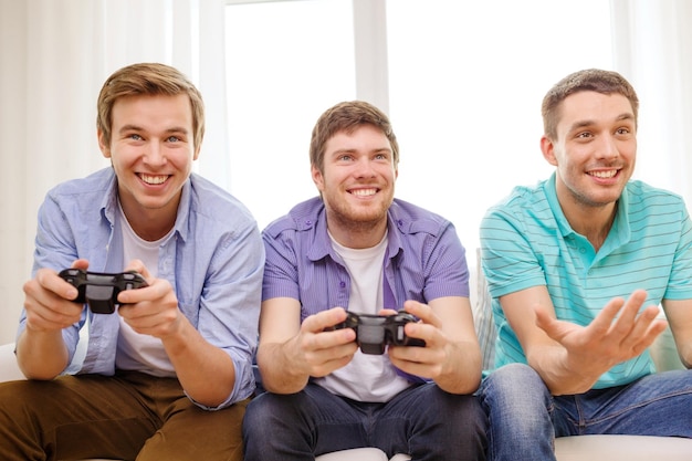 friendship, technology, games and home concept - smiling male friends playing video games at home