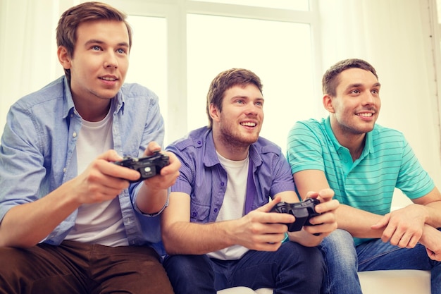 friendship, technology, games and home concept - smiling male friends playing video games at home