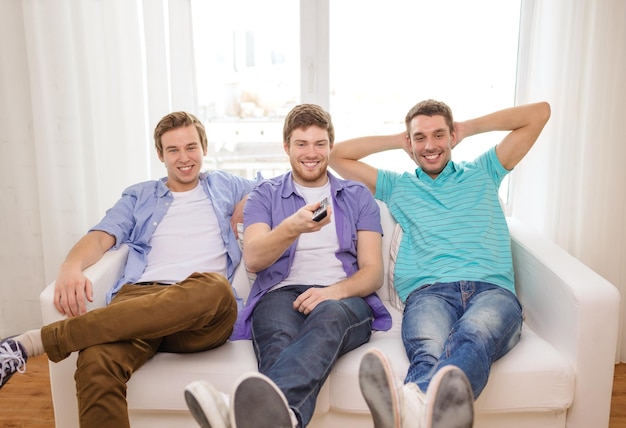 friendship, technology and home concept - smiling male friends with remote control at home