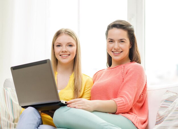 Friendship, technology and internet concept - two smiling teenage girls with laptop computer at home