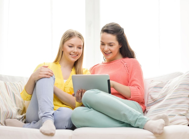 friendship, technology and internet concept - two smiling teenage girls with tablet pc computer at home