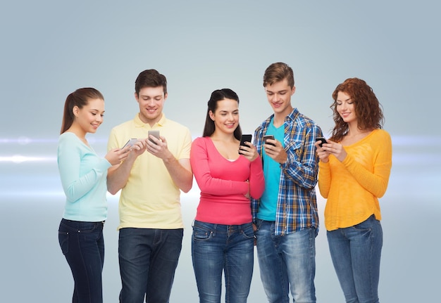 friendship, technology and people concept - group of smiling teenagers with smartphones over gray background with laser light