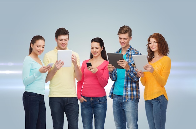友情、技術、人々の概念-レーザー光で灰色の背景にスマートフォンとタブレットPCコンピューターで笑顔のティーンエイジャーのグループ