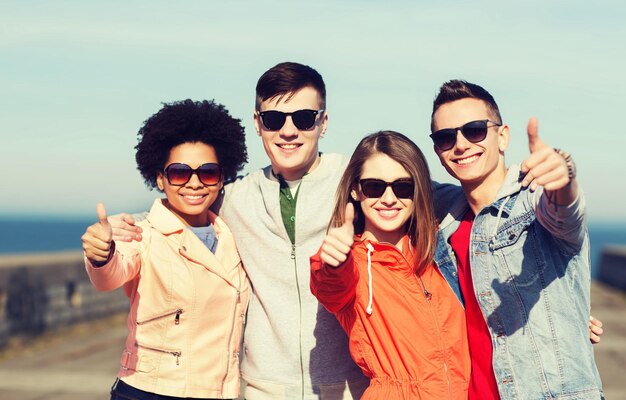Foto concetto di amicizia, turismo, viaggi e persone - gruppo di amici adolescenti felici in occhiali da sole che si abbracciano all'aperto