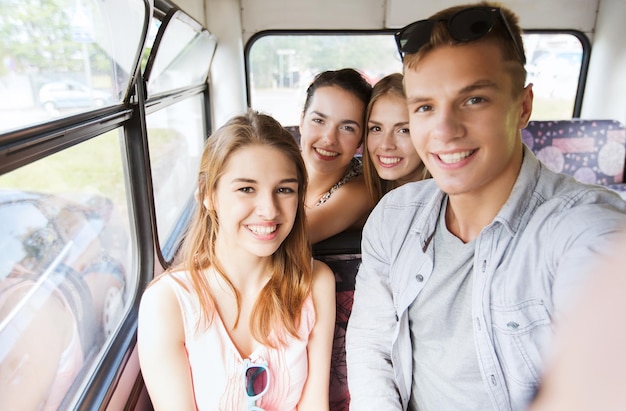 friendship, travel, vacation, summer and people concept - group of happy teenage friends with smartphone traveling by bus