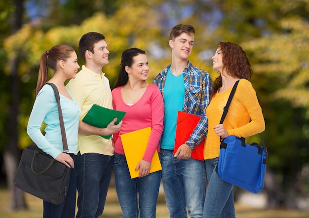 дружба, отдых, образование и концепция людей - группа улыбающихся подростков с папками и школьными сумками на фоне парка