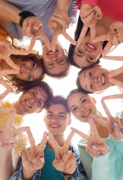 friendship, youth, gesture and people - group of smiling teenagers in circle showing victory sign