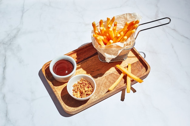 Frieten in een metalen mand op houten dienblad met saus en friet in fel zonlicht fastfood concept