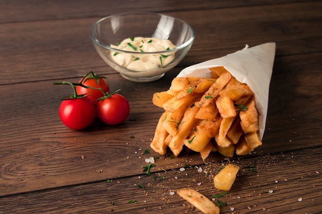 Frieten, in een papieren zak op een houten bruine achtergrond, close-up. Fast food.