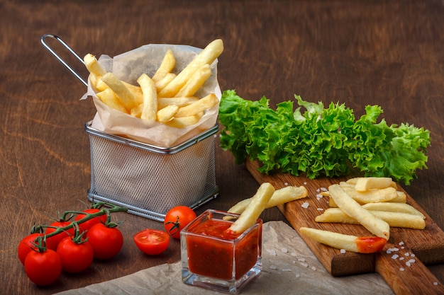 Frieten in een rooster met ketchup, salade en cherrytomaatjes op houten bruine tafel