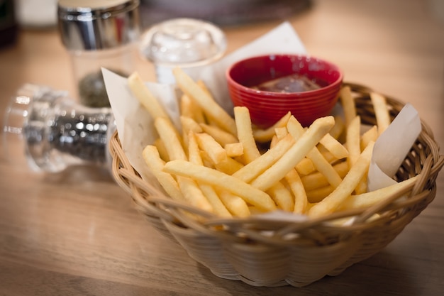 Foto frieten in houten mand met saus en kruiden op tafel.