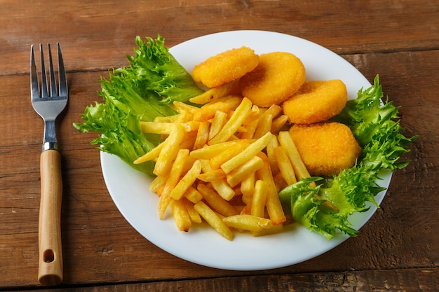 Frietjes met kipnuggets in een bord met kruiden naast een houten tafel naast een vork. Horizontale foto